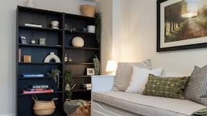 A living room with a dark blue bookshelf, a white sofa with patterned cushions, and a framed painting on the wall.