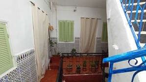 A narrow staircase with a red-tiled floor, green shutters, and potted plants on the landing. - The bird house (Tlemcen)