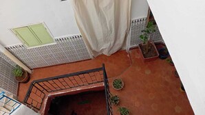 A balcony with a tiled floor, a metal railing, a beige curtain, and several potted plants. - The bird house (Tlemcen)
