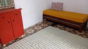 A small room with a bed, a red cabinet, and a patterned rug. - The bird house (Tlemcen)