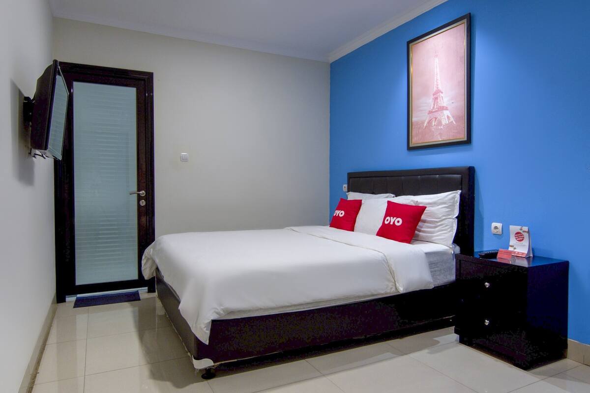 A bedroom with a bed, a nightstand, a framed picture of the Eiffel Tower, and a door with a towel hanging on it.