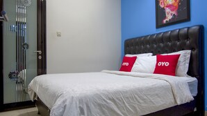 Een netjes opgemaakt bed met witte beddengoed en twee rode kussens met 'OYO'-branding, een zwart gestoffeerd hoofdeinde en een glazen deur met decoratieve details.