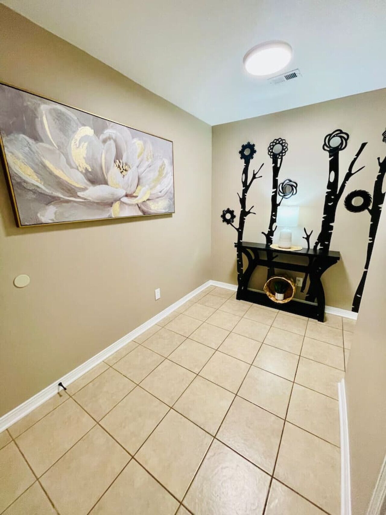 A hallway with beige walls, a large abstract painting, and a black decorative wall piece.
