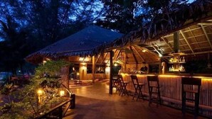 An outdoor bar area with wooden furniture and a thatched roof structure. - Rimba Resort - Dive Centre and Spa (Sibu Island)