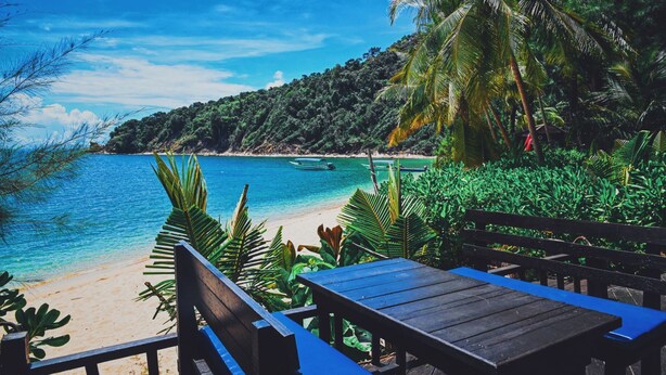 A beach with a wooden bench and table, surrounded by lush greenery and a clear blue sea. - Rimba Resort - Dive Centre and Spa (Sibu Island)