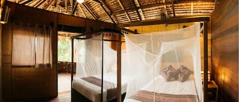 A room with a thatched roof, wooden walls, and a bed with a mosquito net.