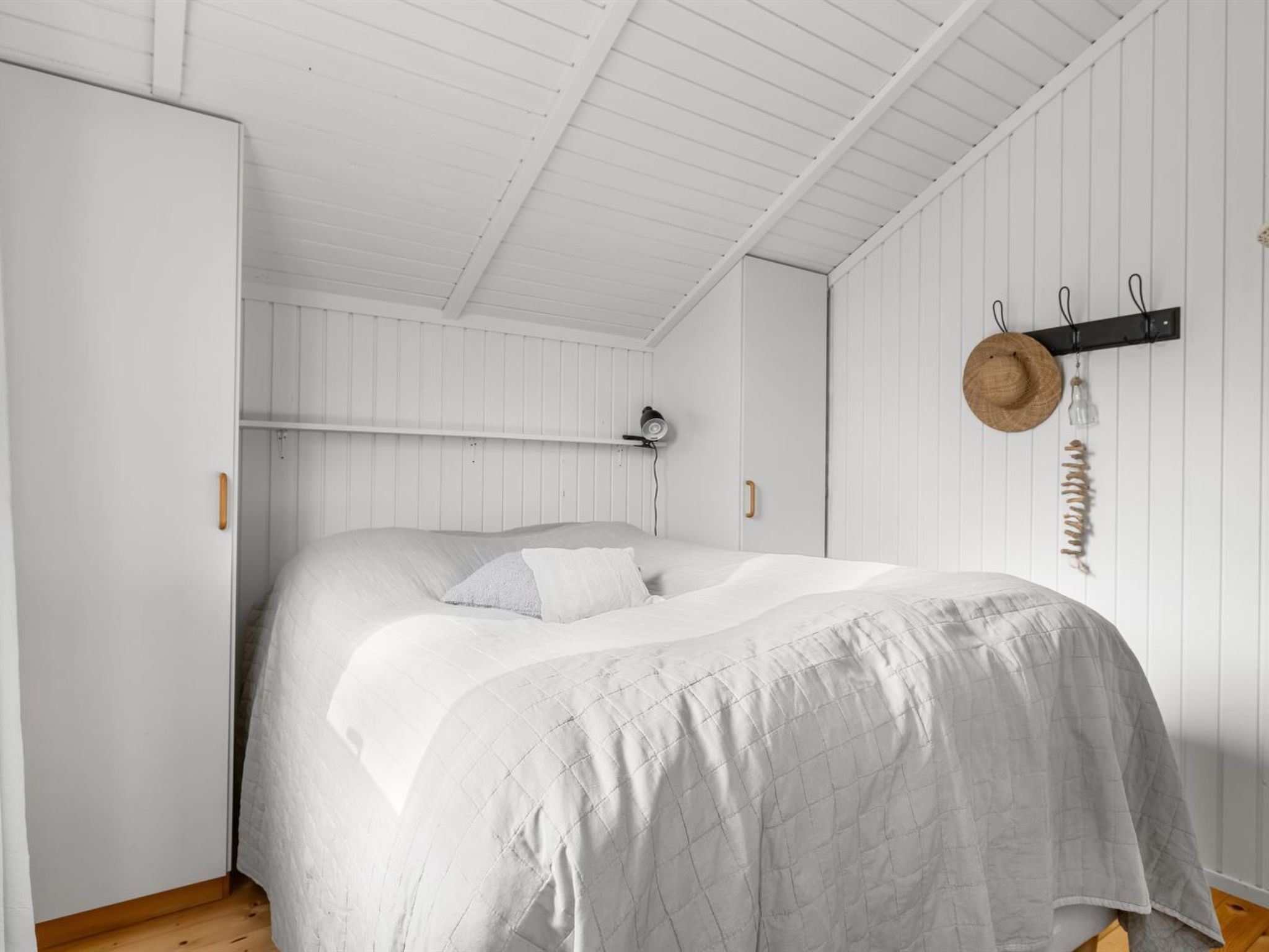 Une chambre à coucher avec un lit, des murs blancs, des poutres en bois au plafond et un chapeau accroché au mur.