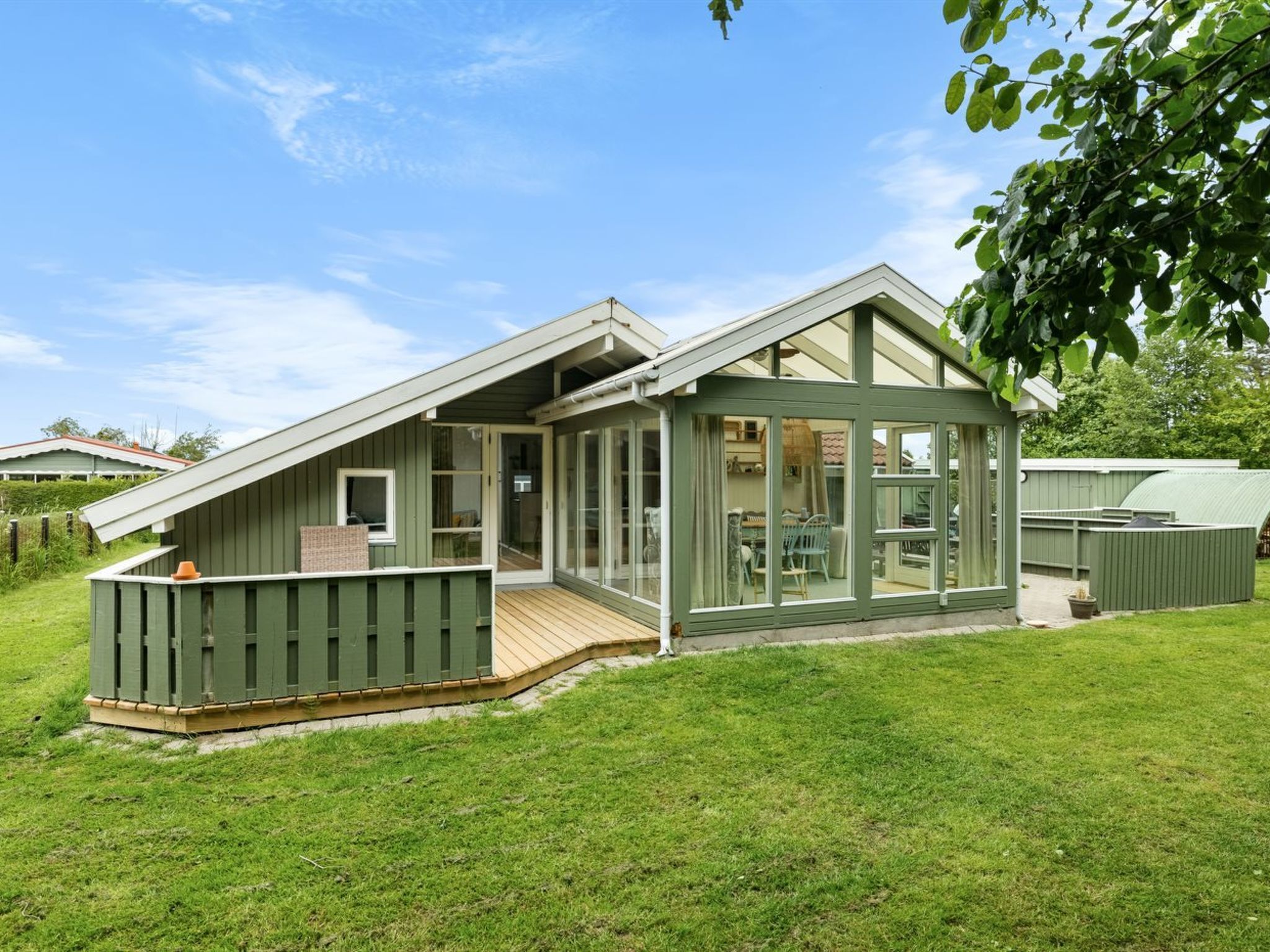 A green-roofed house with a deck and a glass-enclosed porch.