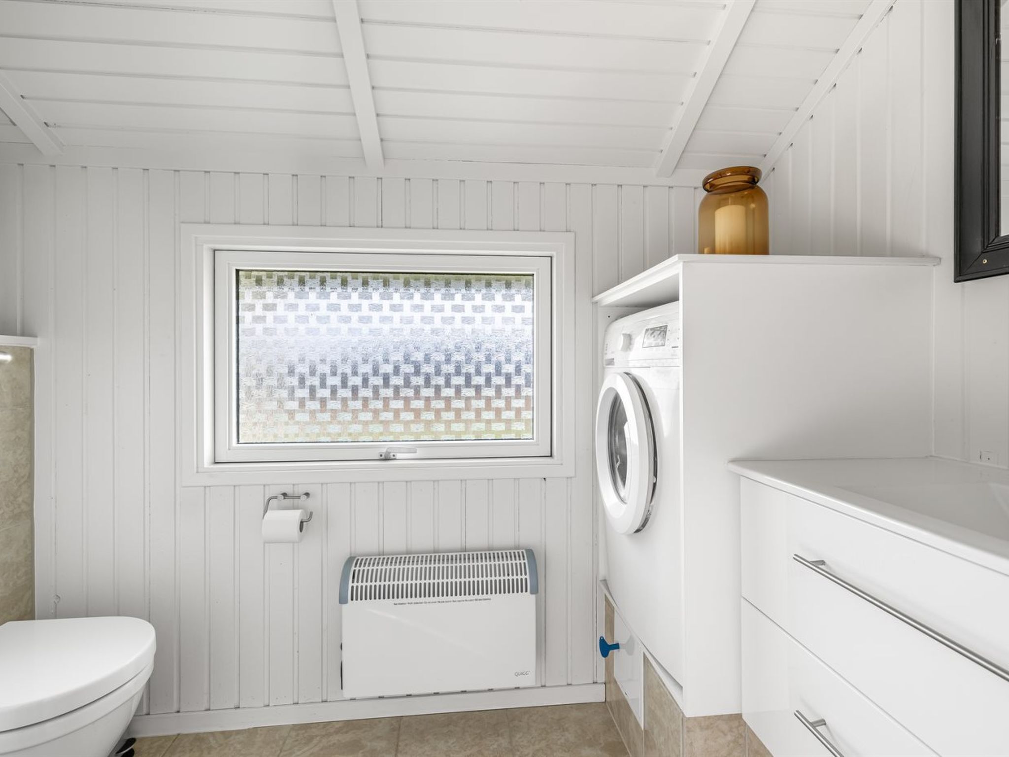 Une petite buanderie comprenant un lave-linge, un radiateur et une fenêtre à carreaux.