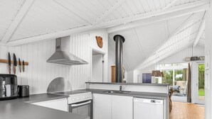 Une cuisine moderne avec des meubles blancs, une cuisinière et un lave-vaisselle. Une grande fenêtre offre une vue sur l’extérieur.