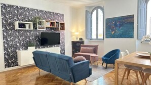 A modern living room with a blue sofa, a pink sofa, and a dining table with chairs. There is a TV mounted on the wall and a painting above the table. - La Bella Vita Navona (Roma)