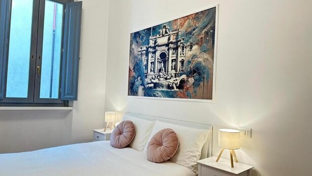 A hotel room with a large bed, two bedside tables with lamps, a window with blinds, and a painting on the wall. - La Bella Vita Navona (Roma)