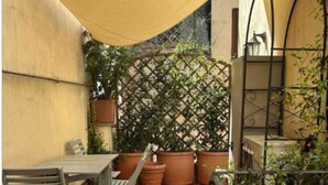 A patio with a table and chairs, surrounded by potted plants and a yellow shade sail. - La Bella Vita Navona (Roma)
