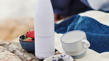 A white water bottle labeled "VILLA MARSTRAND" on a table with a bowl of strawberries, a bowl of blueberries, and a white mug.