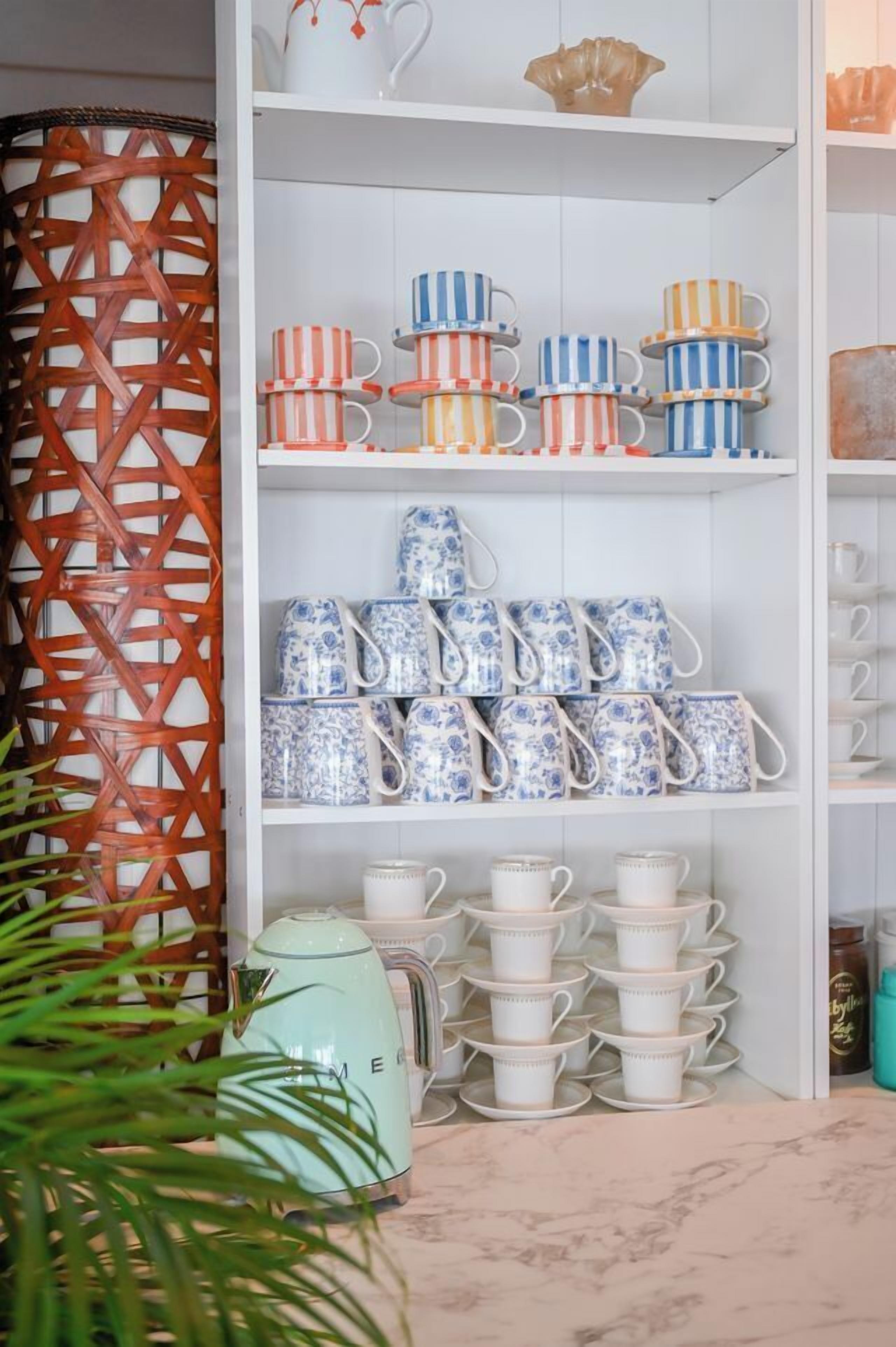A kitchen with white shelves holding various kitchenware, including striped cups and floral-patterned mugs.