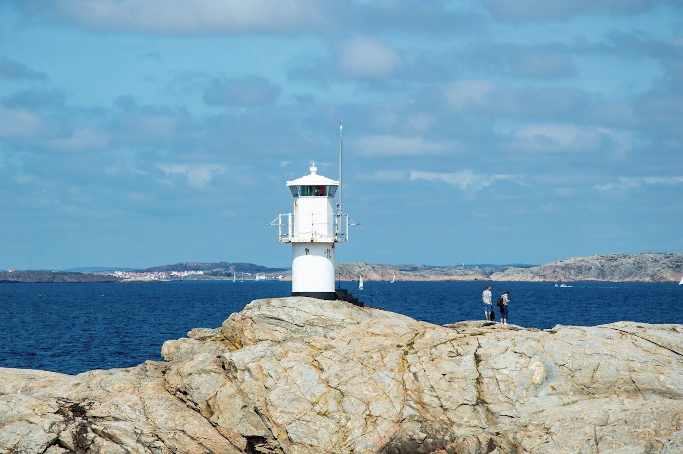 A lighthouse on a rocky outcrop with a clear view of the sea and distant land.