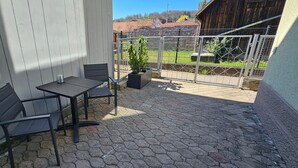 An outdoor patio with a table and chairs, a potted plant, and a view of a fenced area with a building in the background. - Elodia Luxury Apartment - Wi-Fi, Smart TV, Terrace, Kitchen, Towels (Heidenheim an der Brenz)