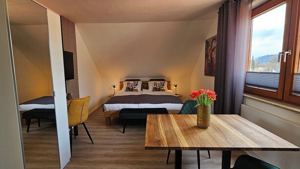 A compact bedroom with a bed, bedside tables, a small table with a vase of flowers, and a window with curtains. - Elodia Luxury Apartment - Wi-Fi, Smart TV, Terrace, Kitchen, Towels (Heidenheim an der Brenz)