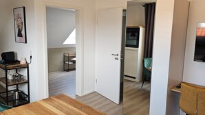 A modern room with a wooden dining table, a TV mounted on the wall, and a kitchen area visible through an open door. - Elodia Luxury Apartment - Wi-Fi, Smart TV, Terrace, Kitchen, Towels (Heidenheim an der Brenz)