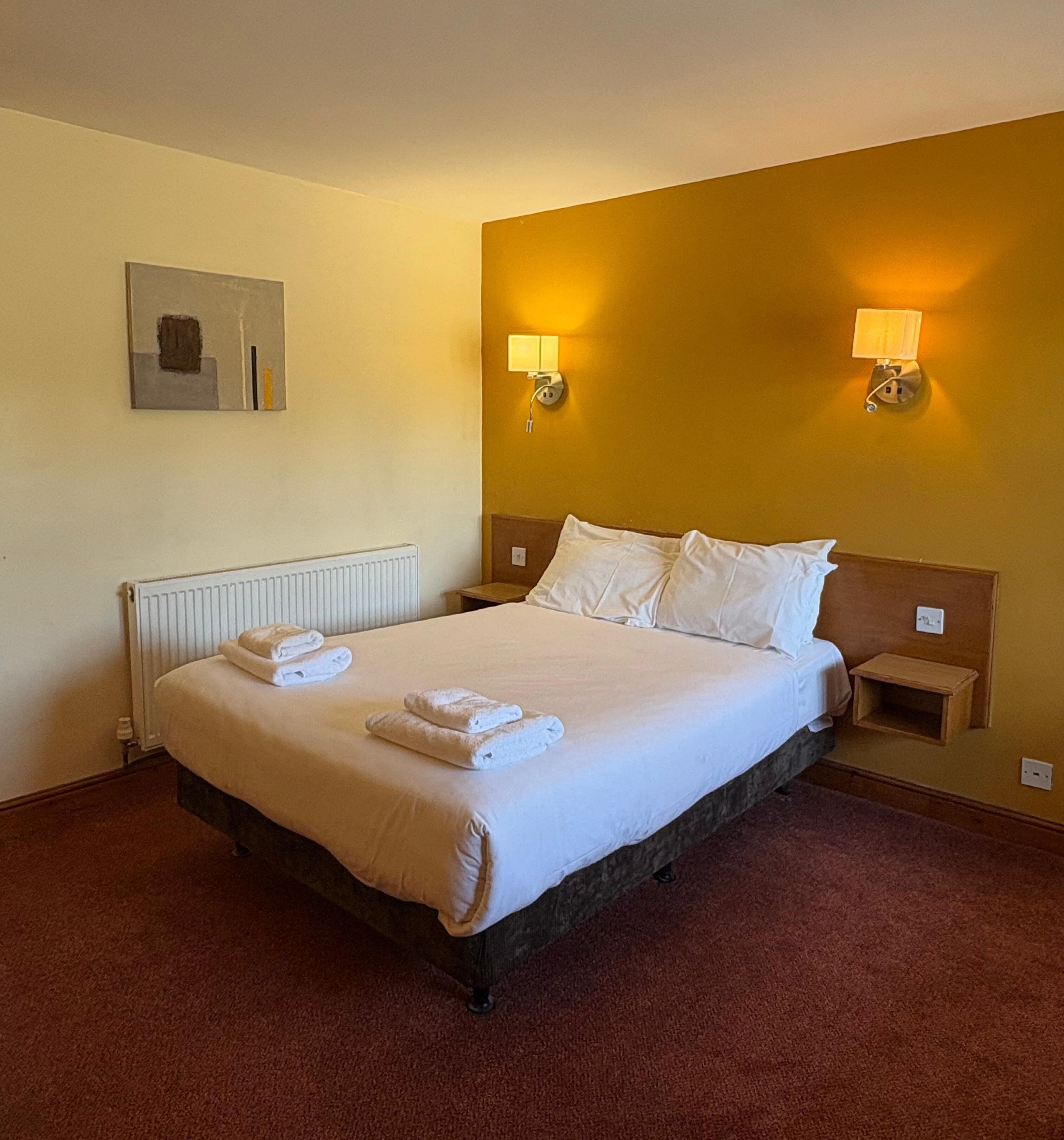 Une chambre d’hôtel avec un lit, deux lampes de chevet, un radiateur et une petite table de chevet.