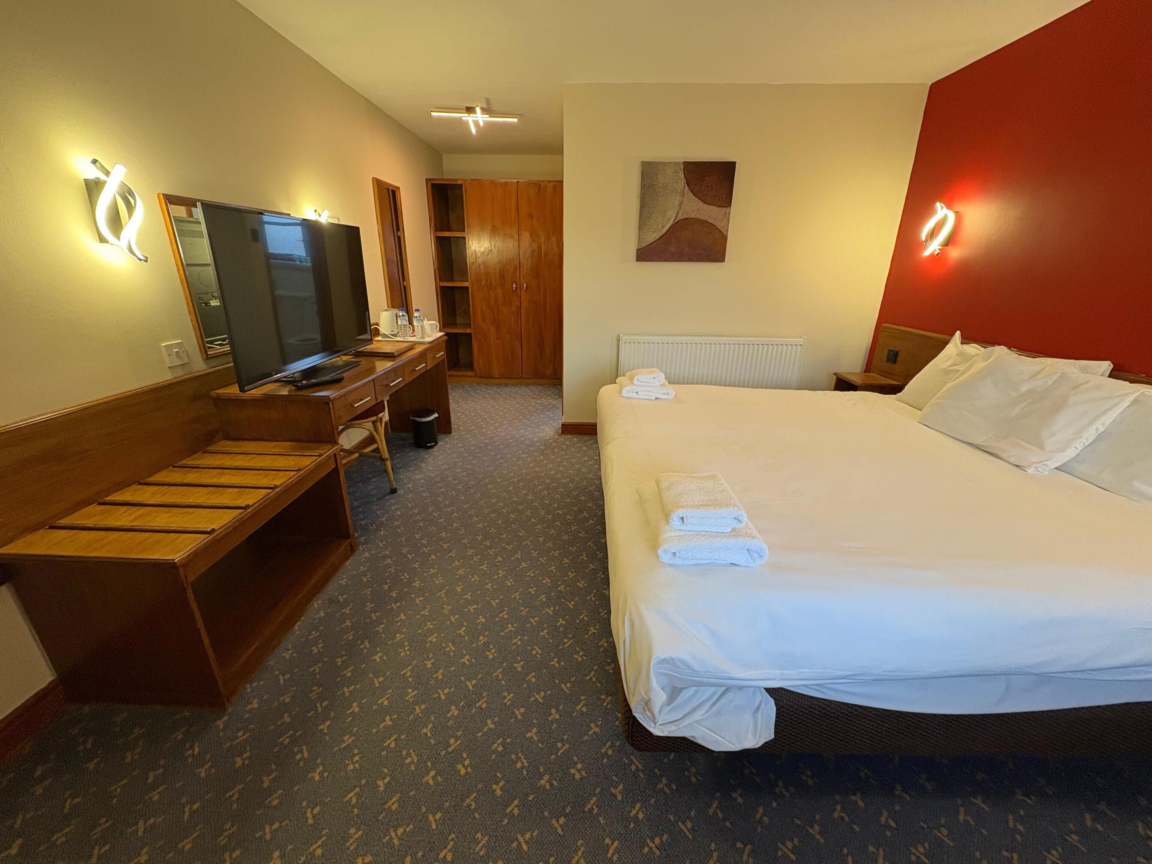 Une chambre d’hôtel comprenant un lit, un bureau avec un ordinateur, une télévision et une armoire.