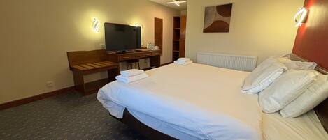 Een hotelkamer met een groot bed, een televisie, een bureau met stoel en een radiator.