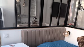 Interior compacto de una caravana con cama, un mueble blanco pequeño y una ventana.