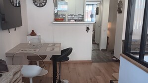 Una cocina moderna con armarios blancos, un comedor con mesa y sillas blancas, y una sala de estar con piso de madera y un ventanal grande.