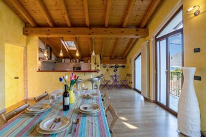 A dining area with a wooden ceiling, a kitchen in the background, and a view through large glass doors.