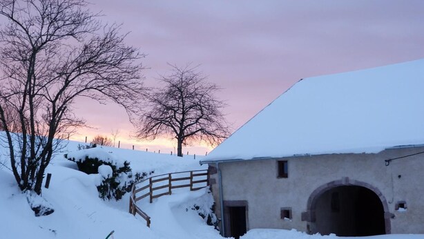 Un bâtiment recouvert de neige, avec une clôture en bois et une entrée en forme de tunnel.