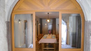 Un coin repas avec une table en bois dressée pour quatre personnes, flanqué de portes vitrées donnant sur une cuisine et une autre pièce.