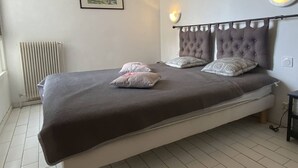 A bed with a headboard, pillows, a framed picture on the wall, and a wall-mounted light fixture.