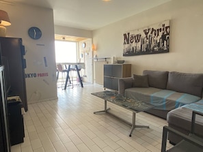A living room with a sofa, a coffee table, a clock, and a wall with a 'New York' poster.