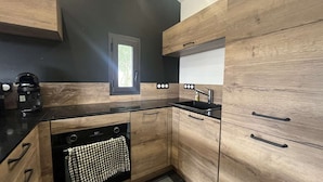 A modern kitchen with wooden cabinets, a black countertop, and a window with a view of greenery.