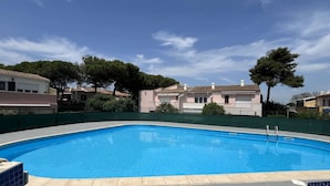 A swimming pool with a tiled edge, surrounded by a green fence, and houses in the background.