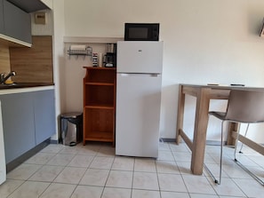 A compact kitchen with a refrigerator, microwave, coffee maker, and a small trash bin.