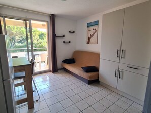 A room with a sofa, a dining table, a cabinet, and a view through a glass door.