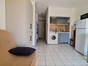 A compact living space with a kitchenette, a washing machine, and a bed with a pillow.