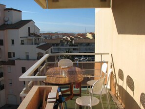 Ein Balkon mit einem runden Holztisch, zwei weißen Stühlen und einem Metallstuhl.