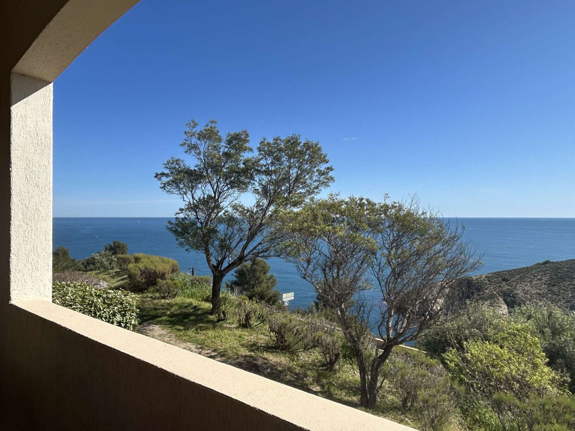 En balkon med udsigt over havet, træer og et stykke klippeagtigt landskab.