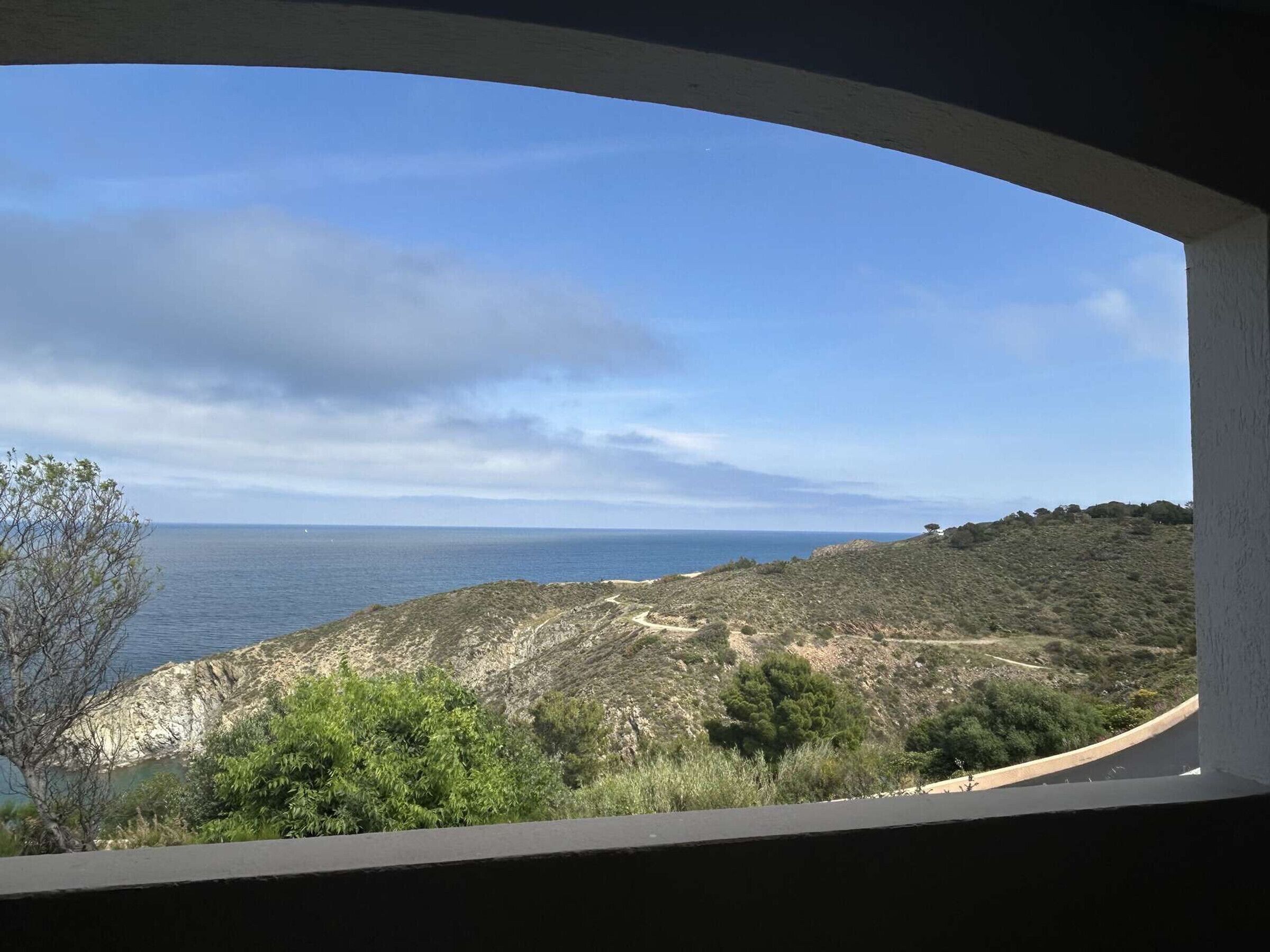 A coastal view through a window, including a clear sky, sea, and hilly terrain.