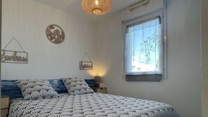 A bedroom with a bed, a hanging light fixture, a window with a view, and wall decorations. - Modern 2-room apartment with parking and Wi-Fi in Banyuls-sur-Mer (Banyuls-sur-Mer)