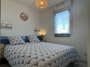 Quarto com cama, luminária pendente, janela com vista e decorações nas paredes.