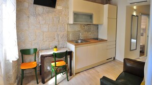 A compact kitchen with a stone wall, wooden ceiling, and a small dining area with two chairs. - Modern Studio in the City Center (Split)