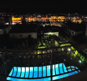 A nighttime view of a cityscape with illuminated buildings and a pool area with a blue-lit edge. - Stunning View Suite With Balcony (Trogir)
