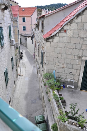 Une rue étroite bordée d’immeubles en pierre, un scooter garé sur le bord et un enfant qui marche.