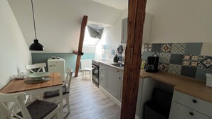 Ett kompakt kök med en matplats, ett vitt kylskåp, en kaffebryggare och en kakelbeklädd vägg bakom arbetsbänken.
