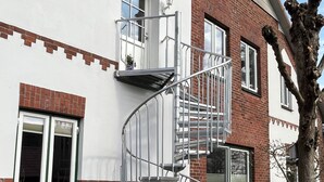 En tvåvåningsbyggnad med en spiraltrappa, en fasad av tegel och vit puts, samt en trädgård med blommor och växter.