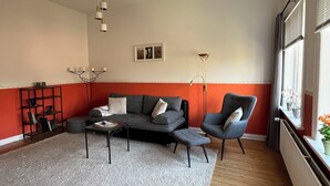 Ett vardagsrum med en grå soffa, en blå fåtölj, ett soffbord, en bokhylla och en golvlampa.