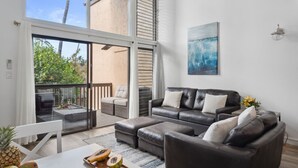 Una sala de estar moderna con un amplio ventanal corredero que da a un balcón, un conjunto de sofás de cuero y una mesa de comedor con fruta.